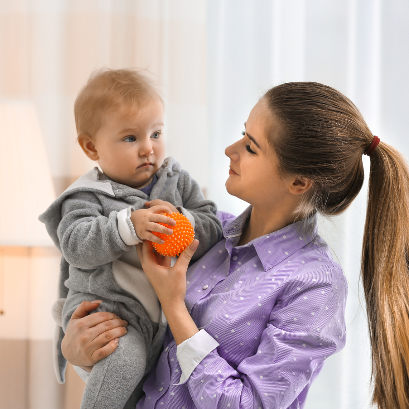 bilingual nanny holding a baby with a ball